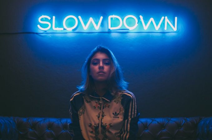 Fashion Language - woman sitting on brown sofa under slow down neon signage